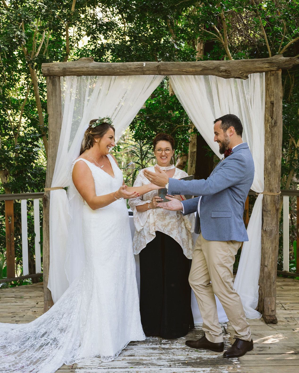 The bride and groom exchanging rings under the arch, Felicity between them holding the ring box, rainforest behind